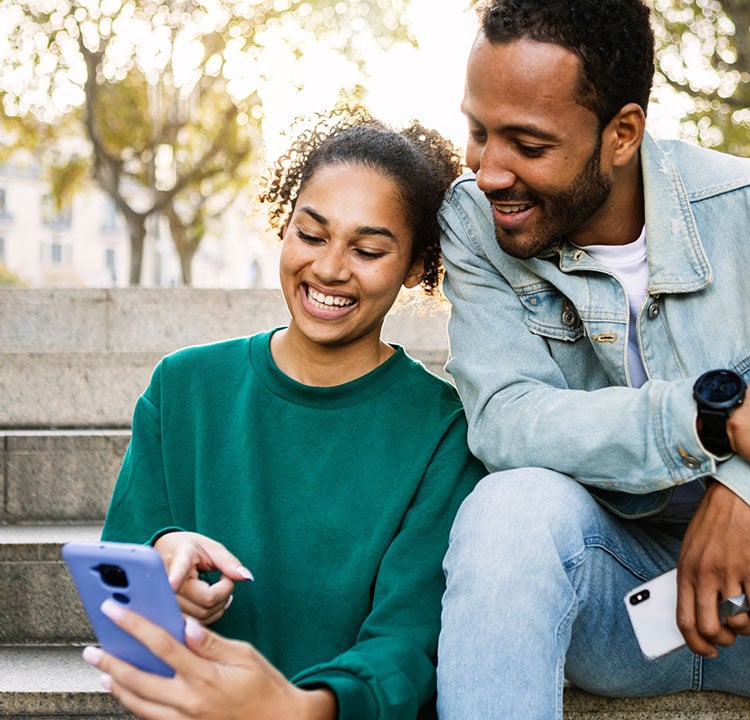 A couple sitting on steps outside looking at a phone and smiling