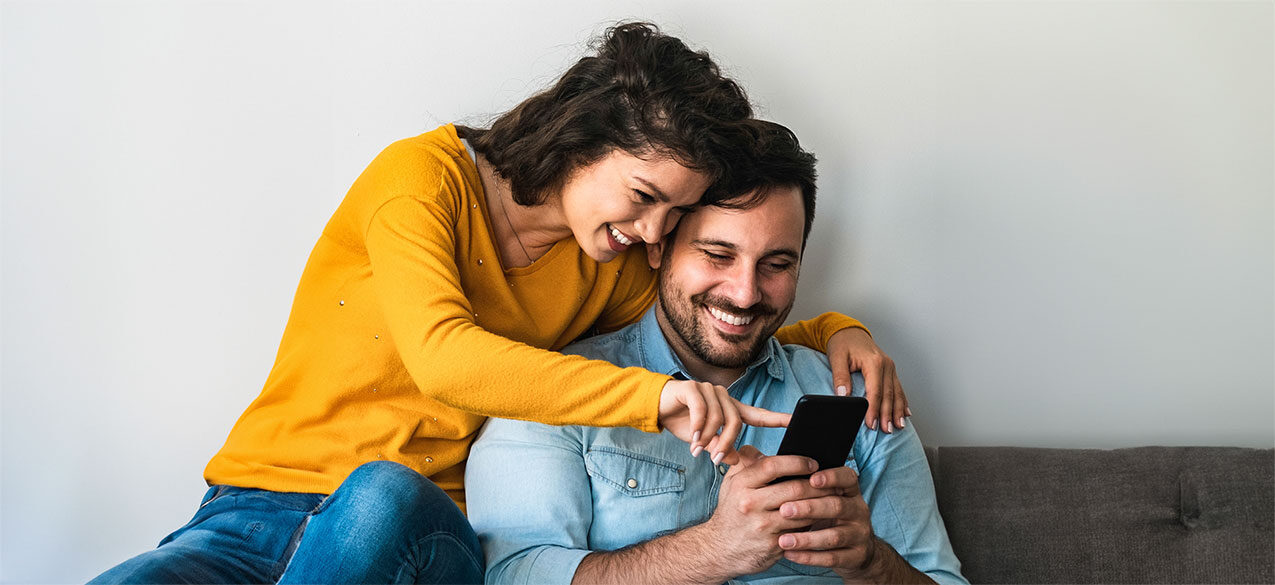 Couple sitting on a couch together looking at the man's phone and smiling