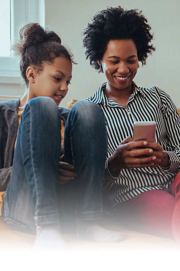 A mother and daughter sitting on a couch looking at the mother's phone