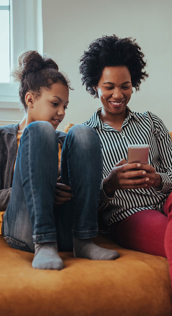 A mother and daughter sitting on a couch looking at the mother's phone